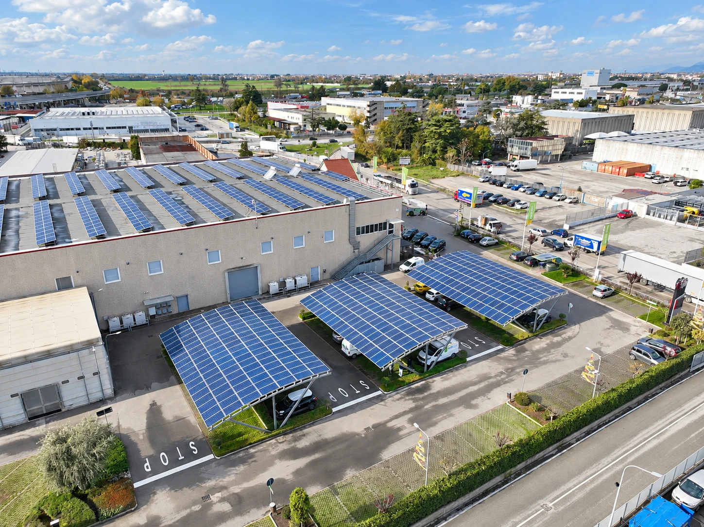 Vista dal drone di tettoie metalliche con pannelli fotovoltaici e capannone industriale.